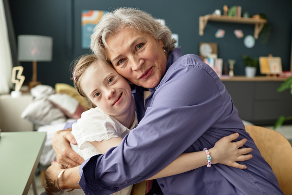 Elderly woman joyfully hugging young girlw ith Down syndrome